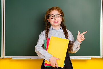 Poster - Photo of small schoolkid girl direct finger empty space wear uniform isolated on yellow color blackboard background