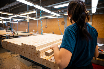 Worker handling stacks of wooden planks in a woodworking factory, preparing materials for further processing under industrial lighting