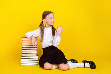 Wall Mural - Full body photo of cute little schoolgirl sit floor books pile point empty space dressed uniform isolated on yellow color background