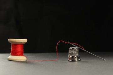 Wall Mural - Sewing needle with red thread and thimble on grey table against black background