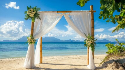 Wall Mural - A beautifully decorated wedding arch stands on a sandy beach, surrounded by clear blue water and distant mountains.