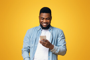 Poster - Smiling african american guy reading message on smartphone over yellow studio background with copy space