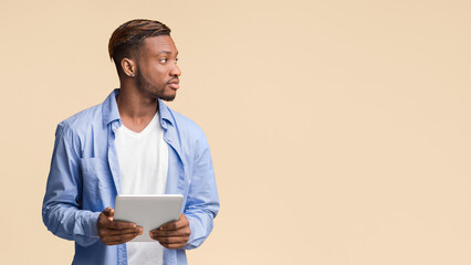 Aufkleber - Serious Afro Guy Holding Digital Tablet Looking Aside Standing Over Yellow Studio Background. Panorama, Copy Space