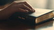 © AnastasiiaRozhmanova - Detailed view of a female hand resting on a closed 'Holy Bible' on a table, symbolizing a deep connection to Christian beliefs. The scene captures the essence of studying God’s wor