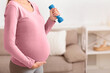 © Prostock-studio - Prenatal Home Training. Closeup of pregnant woman holding dumbbell, touching belly. Free space