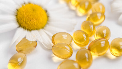 Vitamins in yellow capsules and chamomile, close-up on a white background. Vitamins and healthy lifestyle, capsule yellow tablets isolated on white background. Medicines, vitamin therapy concept