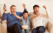 © Prostock-studio - Excited Boy With Father And Grandfather Watching Soccer Match On TV Cheering Favorite Team Sitting On Sofa Indoor.