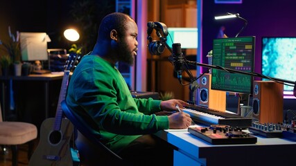 Songwriter taking notes to create new tracks for an album in his home studio, writing lyrics and harmonic elements before recording his song and editing on software, acoustical engineering. Camera A.