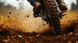 A motocross rider’s close-up of their bike’s rear wheel kicking up dirt and debris, with the rider’s foot and gear in action.


