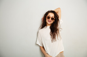 Wall Mural - Relaxing toothy smiling woman posing in fashion sunglasses and white t-shirt on white wall background with empty copy space. Happy lifestyle