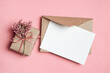 © nikavera - Blank greeting card mockup, white paper card with envelope, gift box and flowers on pink background