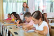 © JackF - Diligent elementary school student tween girl studying with classmates, making notes of teacher lecture