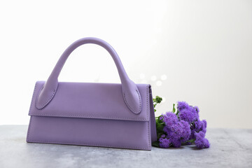 Poster - Stylish violet bag and ageratum flowers on gray table against light background, space for text