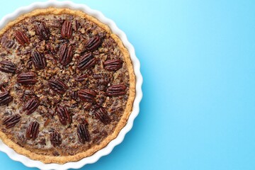 Delicious pecan pie in baking dish on light blue background, top view. Space for text