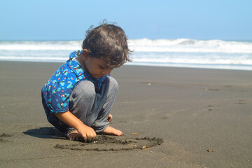 Cute child drawing picture on a sand playing outdoor on summer beach. Boy drawing on sand at seaside. Child drawing sand by imaginary on beach for learning. Kids summer travel and adventure.