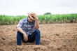 © kamonrat - Contemplative Farmer Sitting on Barren Land, Reflecting on the Challenges of Agriculture, Drought, and the Unpredictability of Nature in a Rural Farm Setting