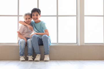 Wall Mural - Little boy with his sister hugging near window