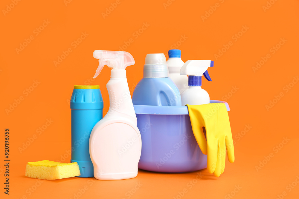 Bowl with different cleaning supplies on orange background
