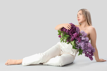 Poster - Young woman with lilac flowers sitting on light background