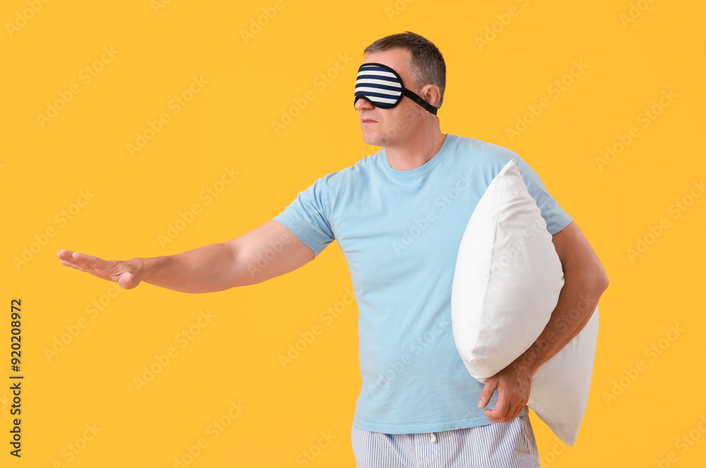 Mature man with sleeping mask and soft pillow on yellow background