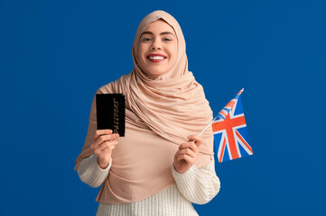 Poster - Beautiful young happy Muslim woman with UK flag and passport on blue background