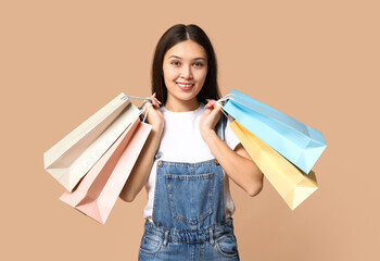 Wall Mural - Fashionable young Asian woman in stylish denim overalls with shopping bags on brown background