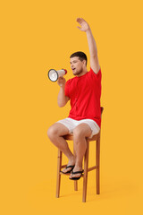 Wall Mural - Young male lifeguard with megaphone sitting on chair against yellow background