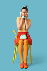 Sticker - Shocked young fashionable woman with retro phone sitting on chair against blue background