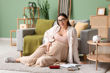 Poster - Pregnant young woman with calculator and notebook sitting on floor in living room