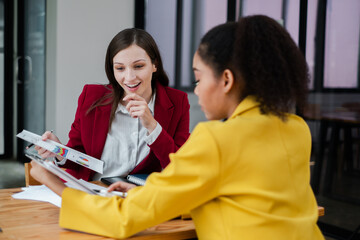 Wall Mural - Two professional women engaged in a business meeting, reviewing documents in a modern office environment.