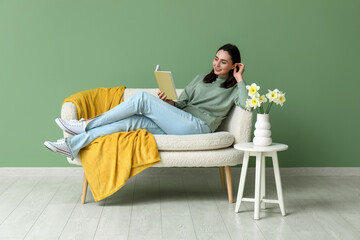 Wall Mural - Young woman reading book on sofa in green living room