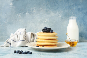 Wall Mural - Plate of sweet pancakes with fresh blueberries, blackberries and bowl of honey on light blue background