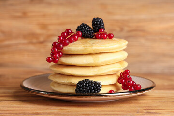 Wall Mural - Plate of sweet pancakes with fresh blackberries and red currants on wooden background