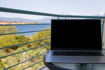 Laptop with blank screen on the balcony overlooking the sea and mountains. summer vacation. work place.