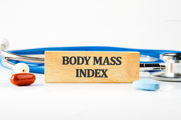 Medical concept. The inscription BODY MASS INDEX on a wooden block with a stethoscope lying next to it, pills, vitamins on a white background