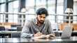 © N7 - An Indian man studying at a table in a library or study area, with a focus on his concentration and the organized study space.