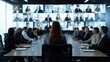 © Usman - A businesswoman sits at the head of a conference table in an office, surrounded by businessmen in suits, with a large monitor hanging above.