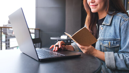 Wall Mural - Closeup image of a young woman writing on a notebook while working on laptop computer