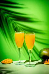 Wall Mural - Summer alcoholic cocktail with champagne, mango juice, syrup and ice, green background, hard light