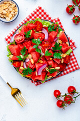 Wall Mural - Juicy salty sweet summer salad with watermelon, tomatoes, onion, peanuts and parsley on white background, top view