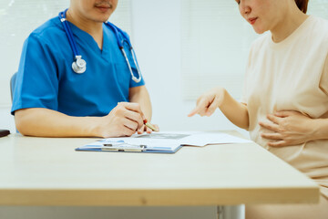 A male Asian pediatrician in a white lab coat conducts a prenatal checkup for a middle-aged pregnant woman, focusing on maternal and fetal health, offering expert care and guidance.