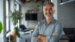 © JINGWEN - Smiling handsome businessman with crossed arms in modern office, middle-aged gray-haired man exuding confidence, business success concept.