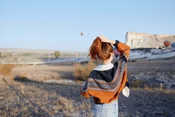 Serene woman with fiery red hair amidst colorful hot air balloons in vast field