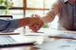 © tynza - Close-up of a handshake between a banker and a client, symbolizing trust and partnership, with financial documents and a laptop on the table.