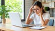 © lililia - A young Korean professional sits at her desk, deeply focused on her laptop, resting her hand on her head while thinking through a complex work challenge