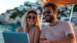 © Pinklife - A cheerful couple wearing sunglasses enjoy a sunny day on a boat while using laptops. The scenic coastal background adds to their joyful and relaxed atmosphere.