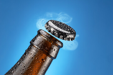 Canvas Print - Opening beer bottle on blue background. Gas cloud going out of the beer bottle blowing the cap.