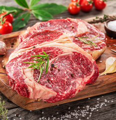 Poster - Raw beef steaks with herbs and spices ready for cooking are on wooden board.