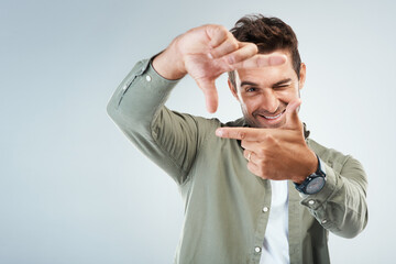 Sticker - Hands, frame and portrait of man in studio with sign for photo, photography or fun picture. Face, male person and influencer on gray background with finger border, selfie smile or wink for confidence