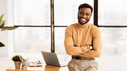 Poster - Successful Salesman. Smiling black man sitting on desk with crossed arms. Panorama, free space